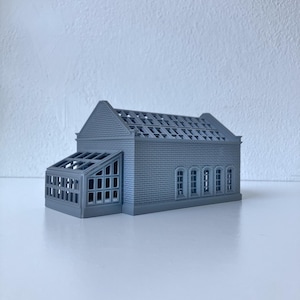 Può includere: Un modello grigio stampato in 3D di un edificio con tetto a capanna e una struttura a serra più piccola annessa. L'edificio principale presenta un esterno con texture a mattoni, finestre ad arco lungo il lato e un tetto a griglia.