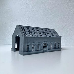 Könnte beinhalten: Ein graues, 3D-gedrucktes Miniatur-Gebäudemodell mit rechteckiger Struktur, Satteldach, mehreren bogenförmigen Fensterrahmen und einer texturierten Ziegeloptik. Das Modell verfügt über einen offenen Eingangsbereich an der Vorderseite.