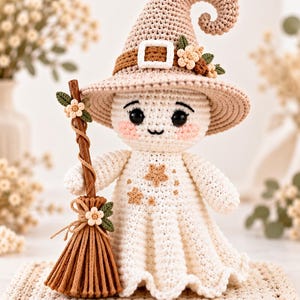 May include: A crocheted ghost doll wearing a beige pointed hat with a brown band, a white buckle, and small flowers. The ghost has black eyes, pink cheeks, and a brown broom with flowers. The body is white with small brown star appliques.