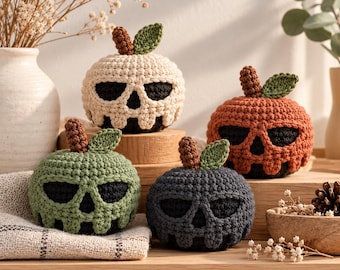 May include: Four crocheted pumpkin-shaped figures featuring skull-like cutouts. Each piece is crafted in a different color: cream, orange, sage green, and dark gray. Every pumpkin has a brown stem and a single green leaf attached to the top.