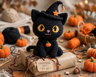 May include: A black crocheted cat wearing a witch hat with an orange star and crescent moon. The cat has large yellow eyes, a pink nose, and a small orange pumpkin charm around its neck. It sits on a brown gift box with a tag reading HANDMADE GIFT for you.