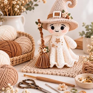 May include: A crocheted ghost doll wearing a beige pointed hat with a buckle and small flowers, holding a brown broomstick. The ghost has black eyes, pink cheeks, and gold star embroidery on its dress. Crafting supplies include yarn, scissors, and buttons.