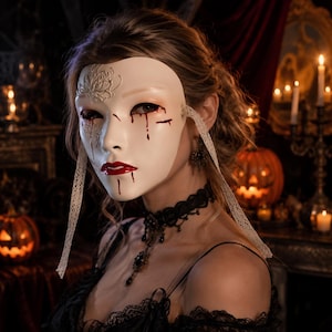 May include: A smooth, off-white face mask featuring a raised floral relief on the forehead, painted red blood-like streaks dripping from the eyes and chin, and bright red lips. The mask is secured with thin, cream-colored lace ribbons on each side.