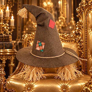 Könnte beinhalten: Ein spitzer Hut aus braunem Stoff mit breiter Krempe, einem Seilband und strohähnlichen Fransen oben und unten. Der Hut ist mit einem einfarbigen roten Quadrat und einem Quadrat mit rot-grün-weißem Karomuster verziert.