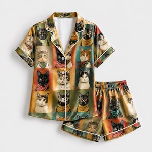 May include: A short-sleeve button-down pajama shirt and matching shorts set featuring a repeating grid pattern of various cat portraits. Each cat is depicted wearing a colorful scarf or bandana against a background of muted earth tones.