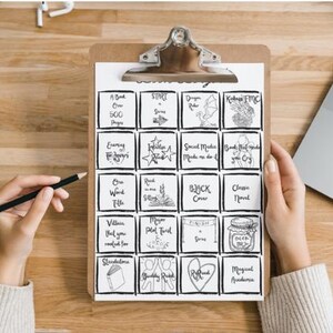 May include: A brown wooden clipboard holding a white paper sheet with a black ink grid of twenty squares. Each square contains hand-drawn illustrations and text prompts for a reading challenge, including phrases like A Book Over 500 Pages, Start a Series, and Magical Academia.