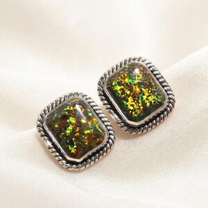 May include: A pair of rectangular stud earrings featuring a dark, iridescent inlay with flecks of green, gold, and orange. Each earring is framed by a silver-toned metal border with a twisted rope texture along the outer edge.