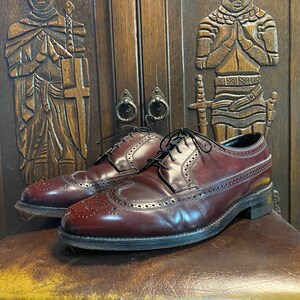May include: Two pairs of burgundy leather wingtip shoes with brogue detailing. The shoes are laced and have a polished finish.