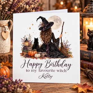 May include: A square greeting card featuring a witch in a black dress and hat sitting with a black cat, a broom, pumpkins, and a lantern under a full moon. The text reads Happy Birthday to my favourite witch Kelly in elegant purple script.
