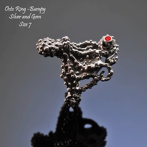 May include: A silver octopus ring with a red gem. The ring is bumpy and textured. The text "Octo Ring - Bumpy Silver and Gem Size 7" is visible in the image.