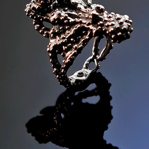 May include: A silver ring with a bumpy texture and a red gem. The ring is shaped like an octopus and is size 7.