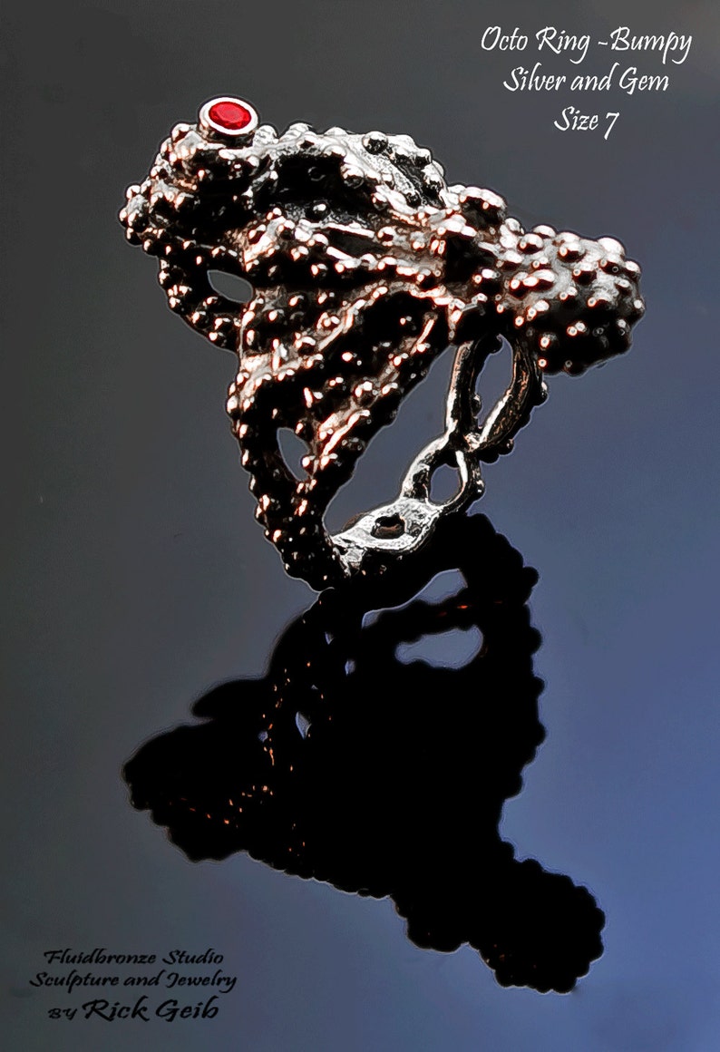 May include: A silver ring with a bumpy texture and a red gem. The ring is shaped like an octopus and is size 7.