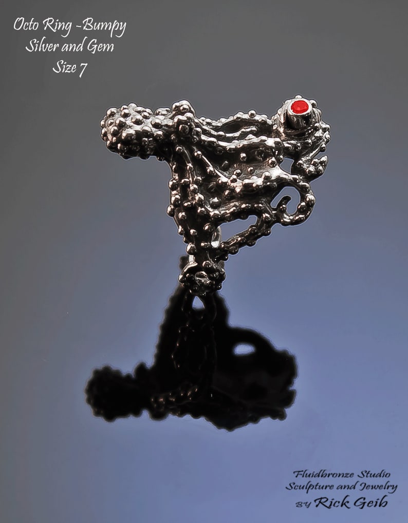 May include: A silver octopus ring with a red gem. The ring is bumpy and textured. The text "Octo Ring - Bumpy Silver and Gem Size 7" is visible in the image.