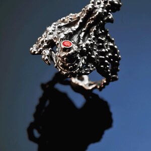 May include: A silver ring with a textured octopus design and a red gemstone. The ring is size 7. "Octo Ring Silver and Gem size 7" is written above the ring.