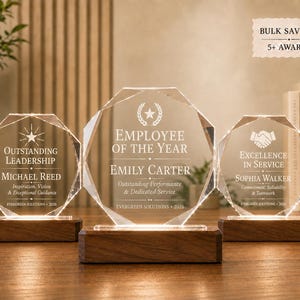 May include: Three octagonal clear acrylic awards with beveled edges, each mounted on a rectangular dark wood base. The awards are engraved with text including "Outstanding Leadership," "Employee of the Year," and "Excellence in Service."