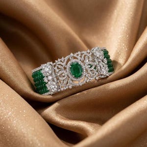 May include: A wide cuff bracelet featuring a central oval-cut green gemstone surrounded by intricate silver-toned filigree metalwork and clear sparkling stones. The sides consist of multiple rows of small, round, deep green beaded strands.