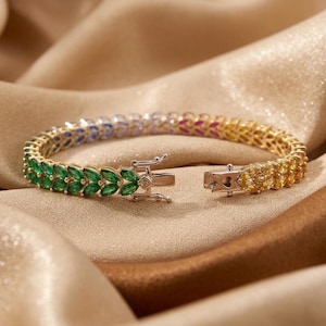 Può includere: Un bracciale metallico caratterizzato da una fila continua di pietre taglio marquise in un gradiente di colori, che sfuma dal verde al blu, al rosa e al giallo. Il pezzo include una chiusura a cassetta in metallo argentato con cerniera.