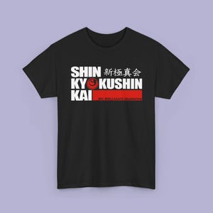 May include: A black short-sleeve t-shirt featuring a white graphic print that reads SHIN KYOKUSHIN KAI with Japanese characters and a red circular logo. Below the text is a red horizontal bar with the text NPO. WORLD KARATE ORGANIZATION.