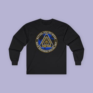 Puede incluir: Una camiseta negra de manga larga con un logotipo circular en el pecho. El logotipo contiene un mapa azul, un triángulo blanco y el texto MUTUAL UFO NETWORK, RAPID RESPONSE SPECIAL UNIT, INVESTIGATION, UFO RESEARCH, MUFON y STAR TEAM.