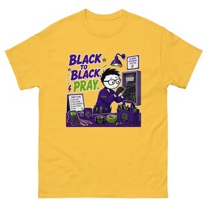 Puede incluir: Una camiseta de color amarillo mostaza con una ilustración de dibujos animados de un electricista trabajando en un panel eléctrico. El gráfico incluye el texto "BLACK TO BLACK. PRAY." junto con herramientas, un multímetro y una lista de tareas.