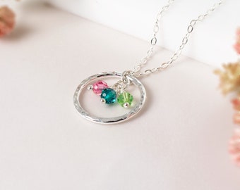 May include: A silver necklace with a hammered circle pendant and three crystal beads in pink, green, and teal.