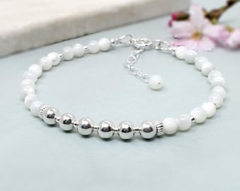 May include: A bracelet featuring a sequence of smooth white beads alternating with polished silver-toned metallic spheres. The design includes a silver-toned chain extension with a small bead at the end, providing an adjustable fit for the wrist.