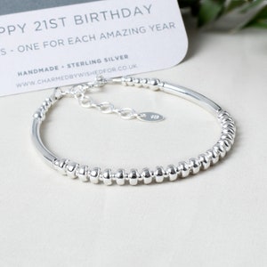May include: Silver bracelet with 21 beads, one for each year. The bracelet has a sterling silver tag with the number 925 on it. The bracelet is on a white surface with a card that says "Happy 21st Birthday - One for each amazing year. Handmade - Sterling Silver www.charmedbywishedfor.co.uk"