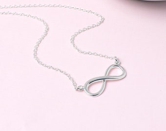 May include: A silver infinity symbol necklace on a delicate chain. The necklace is on a pink background.