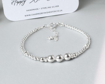 May include: A silver bracelet with three larger beads and smaller beads throughout. The bracelet has a lobster clasp closure. The card in the background says "Happy 30th Birthday!" and "Handmade - Sterling Silver".