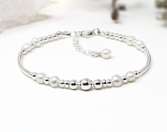 May include: A silver bracelet featuring a repeating pattern of polished silver beads and small white pearls. The design includes a central larger silver bead, a lobster claw clasp, and an adjustable chain extension finished with a single pearl.
