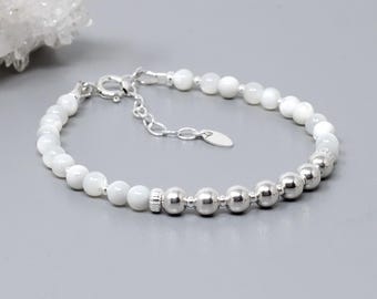 May include: A bracelet featuring a sequence of smooth white beads and polished silver-toned metallic beads. The piece includes a silver-toned lobster claw clasp, a short adjustable chain extension, and a small oval metal tag attached to the closure.