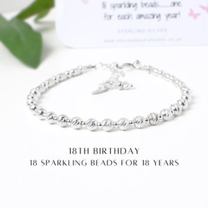 May include: Silver bracelet with 18 small beads, each representing a year. The bracelet has a clasp and a charm. "18th Birthday 18 Sparkling Beads for 18 Years" is written below the bracelet.