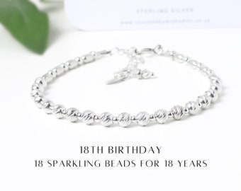 May include: Silver bracelet with 18 small beads, each representing a year. The bracelet has a clasp and a charm. "18th Birthday 18 Sparkling Beads for 18 Years" is written below the bracelet.