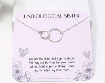 May include: A silver necklace with two interlocking circles, on a pink card with the text "Unbiological Sister" and a message about friendship.