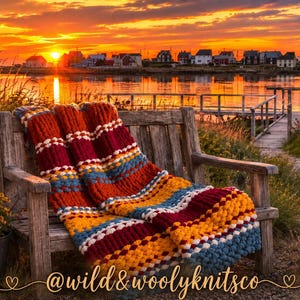 May include: A chunky knit throw blanket featuring horizontal stripes in deep red, mustard yellow, and muted blue, accented with rows of white bobble stitches. The text @wild&woolyknitsco is printed in a cursive script at the bottom of the image.