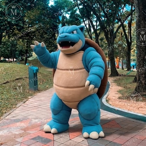May include: A full-body mascot costume of a blue turtle-like creature with a large brown shell on its back. The character features a tan-colored belly, sharp white claws on its hands and feet, and an open mouth showing teeth and a dark interior.