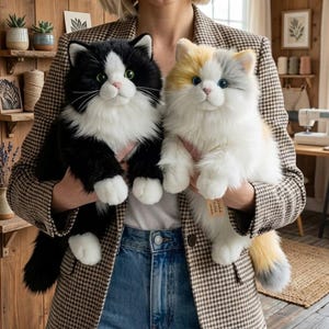 May include: Two plush cat toys with long, soft fur. One cat is black and white with green eyes, and the other is a calico with white, orange, and gray patches and blue eyes. Both stuffed animals have white paws and chest fur.