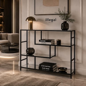 Może przedstawiać: Czarny metalowy stolik konsolowy z geometryczną ramą i kilkoma szklanymi półkami. Na ścianie nad meblem znajduje się napis "illegal" oraz "METALLIST". Stolik jest ozdobiony złotą lampą, książkami i dekoracyjnymi szklanymi misami.