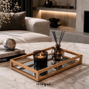 Könnte beinhalten: Ein rechteckiges Tablett aus goldfarbenem Metall mit Spiegelboden, auf dem sich eine dunkelgläserne Kerze mit zwei brennenden Dochten und ein kleiner Glasdiffusor mit schwarzen Stäbchen befinden. Das Tablett hat ein offenes Rahmendesign.