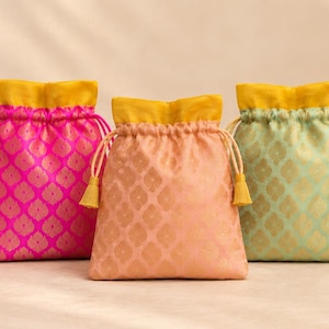 May include: Five drawstring pouches in pink, fuchsia, peach, light green, and yellow. Each bag features a repeating gold leaf-shaped pattern, a solid yellow interior lining, and matching drawstring cords with small tassels at the ends.