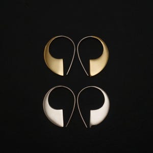 May include: Two pairs of hoop earrings with a teardrop-shaped design. One pair is finished in a matte gold tone, while the other pair is finished in a polished silver tone. Each earring features a thin wire post that curves into a wide, flat base.