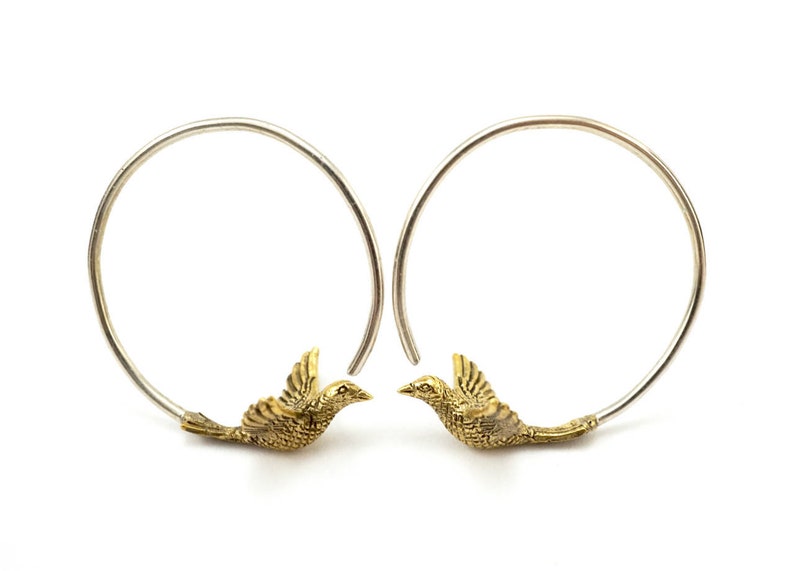 May include: A pair of silver hoop earrings with gold bird charms. The birds are facing each other with their wings spread.