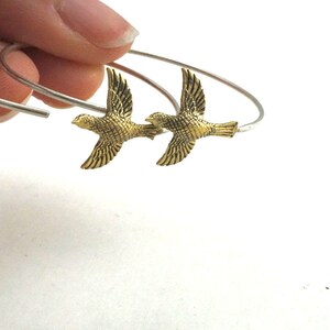 May include: A pair of silver hoop earrings with gold bird charms. The birds are facing opposite directions and have detailed wings.