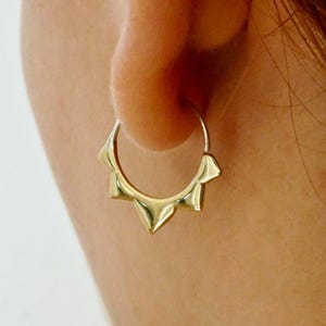 Pode incluir: Uma caneca de cerâmica branca com uma alça preta e o texto "But First, Coffee" em negrito preto. A caneca está sobre um fundo desfocado, sugerindo um ambiente acolhedor.