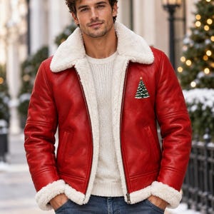 May include: A vibrant red leather jacket featuring a thick white faux-shearling collar and cuffs, worn over a cream-colored cable knit sweater. The jacket displays a small embroidered Christmas tree graphic on the upper left chest area.