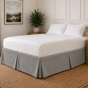 Può includere: Una struttura letto con una gonna plissettata color grigio chiaro che copre la base. Il letto è rivestito con lenzuola bianche pulite e due cuscini bianchi abbinati, creando un aspetto neutro e ordinato per questo elemento d'arredo.