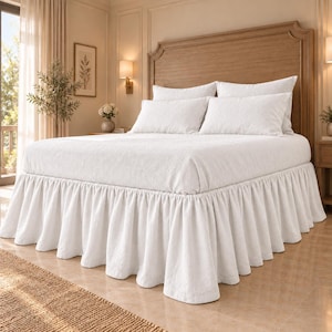 May include: A white bed skirt with a gathered, ruffled design that extends from the base of the mattress to the floor. The fabric features a subtle, textured pattern, providing a clean, uniform look that covers the bed frame and legs.