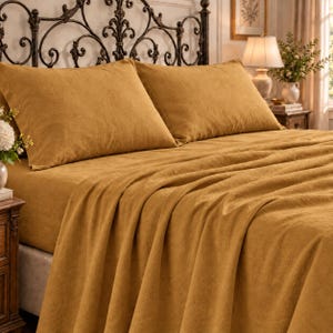 Peut inclure: Un ensemble de linge de lit jaune moutarde comprenant deux oreillers rectangulaires et un drap-housse assorti recouvrant un matelas. Le tissu présente une texture tissée visible, créant un aspect uniforme et uni sur toute la parure de lit.