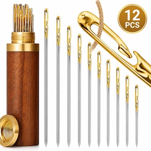 May include: A set of 12 gold-toned self-threading needles with silver shafts, arranged in descending order of size. The needles feature a unique open-eye design and are stored in a cylindrical wooden case with a metallic gold screw-top lid.