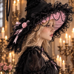 May include: A black pointed hat featuring a wide brim with ruffled black lace trim, a soft pink pleated underside, black beaded drapes, and a decorative pink rose accent with matching ribbons attached to the side of the crown.